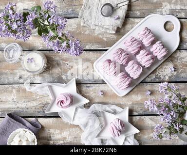 Violett süß hausgemachte Zephyr oder Marshmallow aus schwarzen Johannisbeeren in der Nähe lila Blüten auf Holztisch Top Ansicht in pastellvioletten Farben Stockfoto