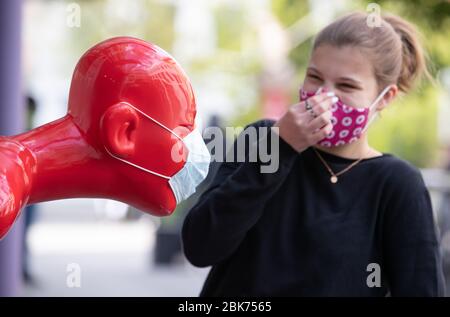 02. Mai 2020, Niedersachsen, Osnabrück: Uschi steht lachend vor einer Skulptur, die einen Mundschutz trägt. Der Laden ihrer Mutter wirbt damit für den Verkauf von Mund- und Nasenschutzmasken. Darüber hinaus leidet das öffentliche Leben unter den Maßnahmen zur Eindämmung der Coronavirus-Pandemie. Foto: Friso Gentsch/dpa Stockfoto