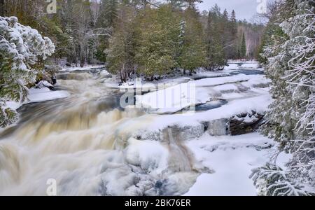 Im Winter nach einem frischen Schneefall, das rauschende Wasser von Egan Rutschen Wasserfall in der Nähe Bancroft, läuft zwischen dem schneebedeckten felsigen Baum gesäumten Ufer. Stockfoto