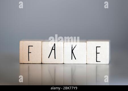 Holzwürfel mit dem Wort Fake auf grauem Hintergrund, Business- und Designkonzept Stockfoto