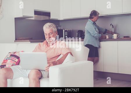 Stayhome und Lockdown Coronavirus Old People Konzept - Senior kaukasischen Paar im Haus in der Küche Kochen und verwenden Sie moderne verbundene Laptop com Stockfoto