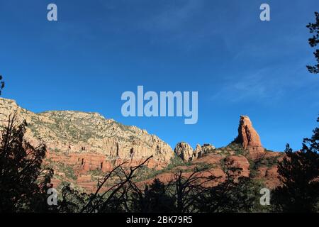 Atemberaubende Felsformationen aus rotem Sandstein und weißem Kalkstein mit Baumsilhouetten im Vordergrund auf dem Brins Mesa Trail in Sedona, Arizona, USA Stockfoto