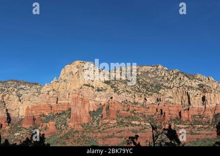 Atemberaubende Felsformationen aus rotem Sandstein und weißem Kalkstein mit Baumsilhouetten im Vordergrund auf dem Brins Mesa Trail in Sedona, Arizona, USA Stockfoto