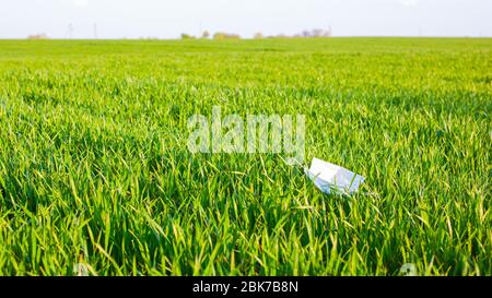 Medizinische Maske auf dem Feld auf dem grünen Gras in der Sonne geworfen. Umweltverschmutzung während der Pandemie des Coronavirus Covid-19. Stockfoto