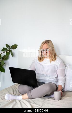 Blonde Frau in Brille arbeiten zu Hause mit Notebook mit Tasse Tee vertikal Stockfoto
