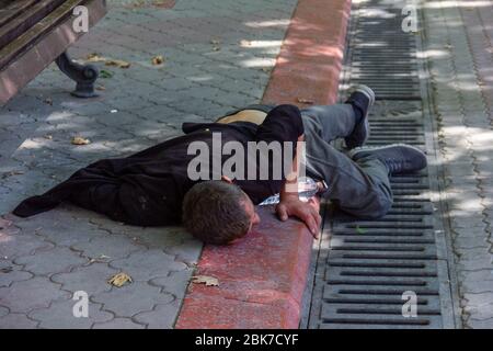 Ein betrunkener Mann liegt an einem Sommertag auf dem Bürgersteig im Zentrum der Stadt Stockfoto