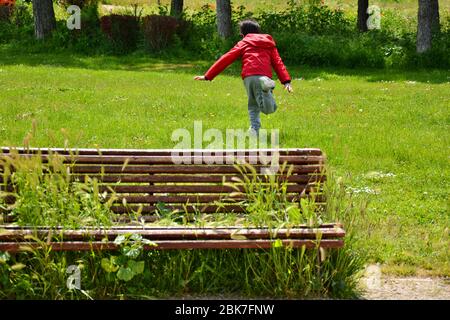 Junger Junge läuft im Park in der Nähe einer Bank voller Pflanzen Stockfoto