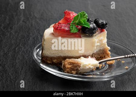 Scheibe cremiger Käsekuchen mit Gelegenbeeren auf schwarzem Steingrund Stockfoto