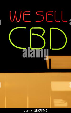 Vertikale Aufnahme von beleuchteten Neon-Fenster Schild mit der Aufschrift "Wir verkaufen CBD" in rot und grün Neon auf der Frontscheibe von Charlotte North Carolina "Head" Shop.