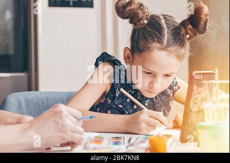 Nette ernsthafte kaukasische Mädchen mit ihrer Mutter zeichnet mit Bleistiften und Farben. Online-Lektionen Stockfoto