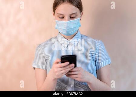 Teenager-Mädchen, Schutzmaske, schreibt Nachricht auf Smartphone, Online-Video-Internet-Anwendung, Anti-Coronavirus COVID-19 Pandemie Infektionskrankheit Stockfoto