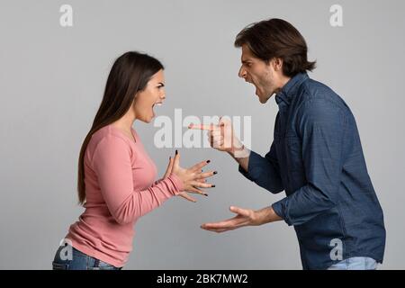 Millennial Paar streiten, schreien und einander vor hellem Hintergrund die Schuld Stockfoto