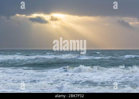 Sonnenstrahlen brechen durch dunkle Wolken über der aufwührenden Nordsee Stockfoto