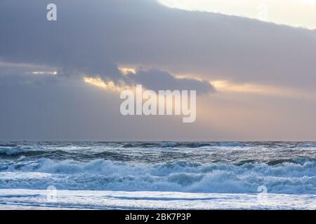 Sonnenstrahlen brechen durch dunkle Wolken über der aufwührenden Nordsee Stockfoto