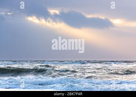 Sonnenstrahlen brechen durch dunkle Wolken über der aufwührenden Nordsee Stockfoto