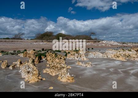 Climping Beach bei Ebbe an einem schönen Frühlingstag mit ungewöhnlichen Steinformationen im Sand. Stockfoto