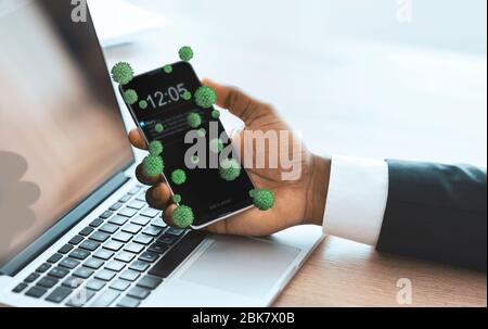 Geschäftsmann hält Smartphone mit Viren auf und arbeitet auf Laptop Stockfoto