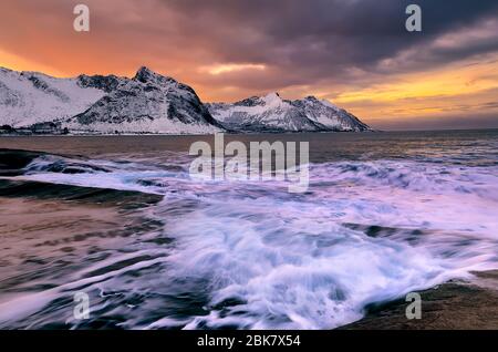 Blick über den Ersfjord von bunten Felsen bei Sonnenuntergang und Felsenbecken bis zu schneebedeckten Bergen an einem dunklen bewölkten Tag, Cape Tungeneset, Senja, Norwegen. Europa. Lang e Stockfoto