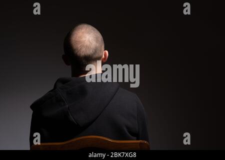 Rückansicht des lässigen kahlen jungen Mannes in schwarzem Hoodie isoliert auf dunklem Hintergrund mit Copyspace Stockfoto