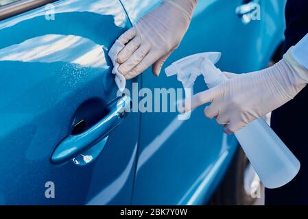 Frau desinfiziert Autotürgriff mit einem antibakteriellen Spray. Autowäsche Stockfoto