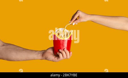 KHARKIV, UKRAINE - 4. APRIL 2020: Nahaufnahme von Mann und Mädchen, die Pommes von McDonald's essen, orangefarbener Hintergrund Stockfoto