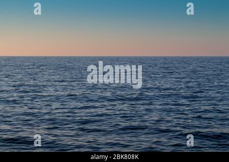 Tiefblaue Farbe des Mittelmeers, mit kleinen Wellen. Blauer Himmel mit pastellfarbenen Rosen und Orange am Horizont. Heraklion, Kreta, Griechenland. Stockfoto