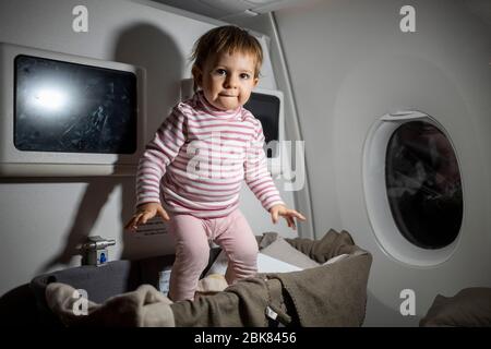 Verletzung der Sicherheitsregeln in einem Flugzeug. Gefahr. Niedliches kleines Kleinkind, das während des Fluges in Babybinde springt. Stockfoto