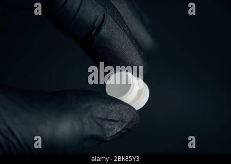 Gelbe Pillen in der Hand halten mit Handschuhen auf dunklem Hintergrund Stockfoto