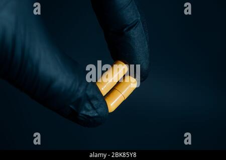 Gelbe Pillen in der Hand halten mit Handschuhen auf dunklem Hintergrund Stockfoto