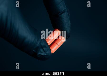 Gelbe Pillen in der Hand halten mit Handschuhen auf dunklem Hintergrund Stockfoto