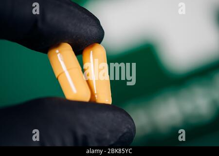 Gelbe Pillen in der Hand halten mit Handschuhen auf dunklem Hintergrund Stockfoto