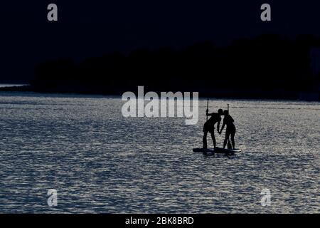 Das Paar paddelt auf den SUP Boards auf dem Meer während der Mondlichtzeit Stockfoto