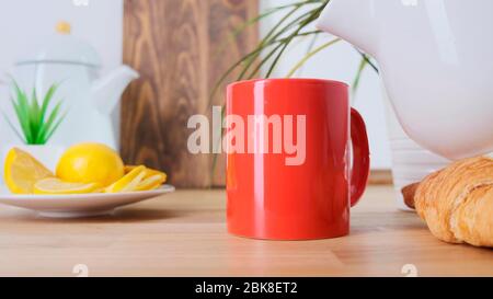 Heißer Kaffee, der in eine rote Tasse auf einem Eichentisch gegossen wird. Nahaufnahme. Stockfoto