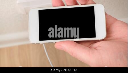 Putin weiß Smartphone auf Ladung. Verbindungskabel zum Telefon. Nahaufnahme. Stockfoto
