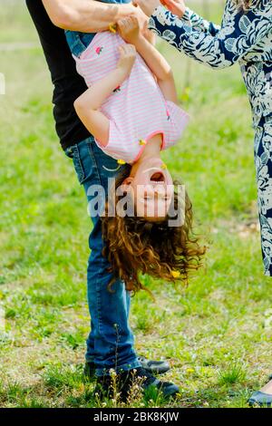 Mama und Papa spielen mit Tochter im Park. Mann hält Kind auf den Kopf. Mädchen lacht mit Eltern spielen. Stockfoto