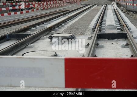 Bau einer Strassenbahnlinie, Einbettung von Metallschienen in einen Betonsockel mit einer Barrieresteele im Vordergrund und an der Seite. Stockfoto