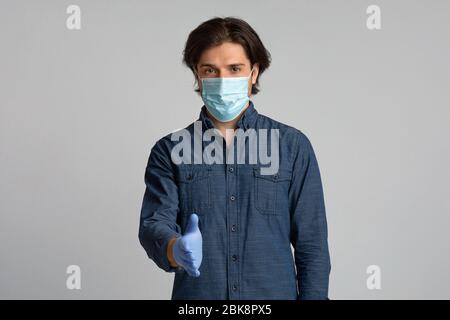 Junger Mann In Medizinischen Maske Und Handschuhe Ausstreckende Hand Für Handshake Stockfoto