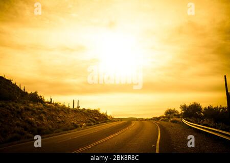 Ein strahlender Sonnenaufgang über einer Straße auf einem Hügel mit saguaro Kakteen an den Seiten der Straße in Arizona. Stockfoto