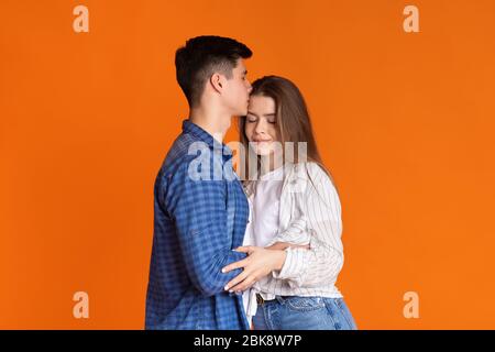 Guy küsst Mädchen in der Stirn auf orangefarbenem Hintergrund Stockfoto