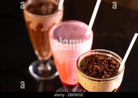 Drei Gläser verschiedener Milchshakes (Schokolade, Erdbeere und Vanille) auf Holzhintergrund Stockfoto