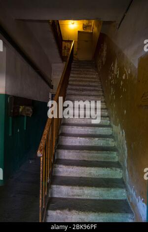 Eine gebogene, dunkle, beängstigende, steinerntete Treppe in einem Wohnhaus aus der kommunistischen Ära der UdSSR. In Vilnius, Litauen. Stockfoto