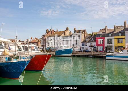 Boote, die am Hafen von Weymouth festgemacht sind, mit Geschäften und Häusern im Hintergrund, an einem sonnigen Sommertag in Dorset, England Stockfoto