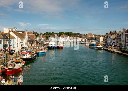 Der malerische Hafen von Weymouth, gesäumt von vertäuten Fischerbooten und Segelbooten, an einem sonnigen Sommertag in Dorset, England Stockfoto