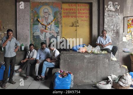 Männer in Mumbai, Maharashtra, Indien, die Zeit in einer dunklen Unterführung vor einem Gewand Bild des Hindu-heiligen Sai Baba von Shirdi aus dem 19. Jahrhundert verstreichen Stockfoto