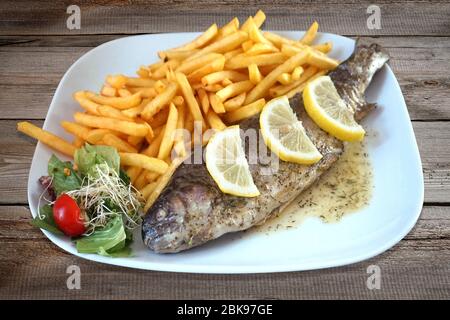 Gebackener Fisch - Forelle, Salat und pommes frites auf dem Teller Stockfoto