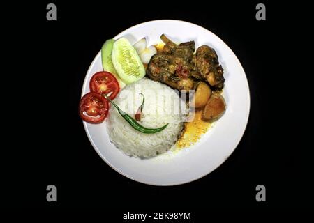 Tasse gekochter Reis mit Hühnerbrühe auf einem weißen Teller auf schwarzem Hintergrund isoliert. Gekochter Reis auf einem weißen Teller, Chili, Tomaten, Gurke. Stockfoto