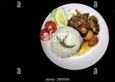 Tasse gekochter Reis mit Hühnerbrühe auf einem weißen Teller auf schwarzem Hintergrund isoliert. Gekochter Reis auf einem weißen Teller, Chili, Tomaten, Gurke. Stockfoto