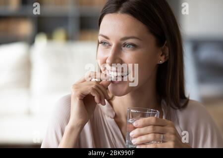 Nahaufnahme lächelnde Frau, die Pille nimmt, hält Wasserglas Stockfoto