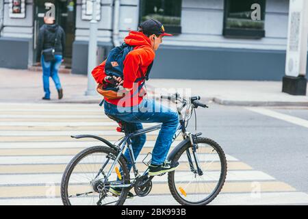 Moskau, Russland - 7. JULI 2017: Ein junger Mann in einem roten Hoodie überquert eine Fußgängerüberfahrt auf einem Fahrrad ohne Hände Stockfoto