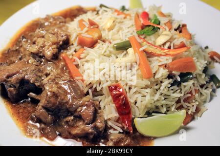 Gemüse gebratener Reis mit Chili-Huhn auf weißem Teller auf gelbem Tuch isoliert. Draufsicht. Chili Chicken ist ein beliebtes indo-chinesisches Gericht Stockfoto